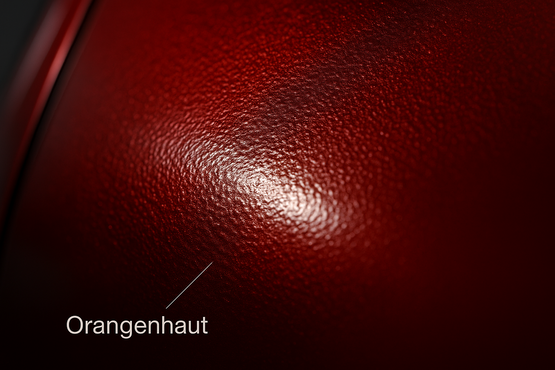 Eine Nahaufnahme von glänzendem, tiefrotem Lack, der eine unebene, feinkörnige Textur aufweist, die an die Oberfläche einer Orangenhaut erinnert. Ein heller Lichtreflex betont die dreidimensionale Struktur des Materials.